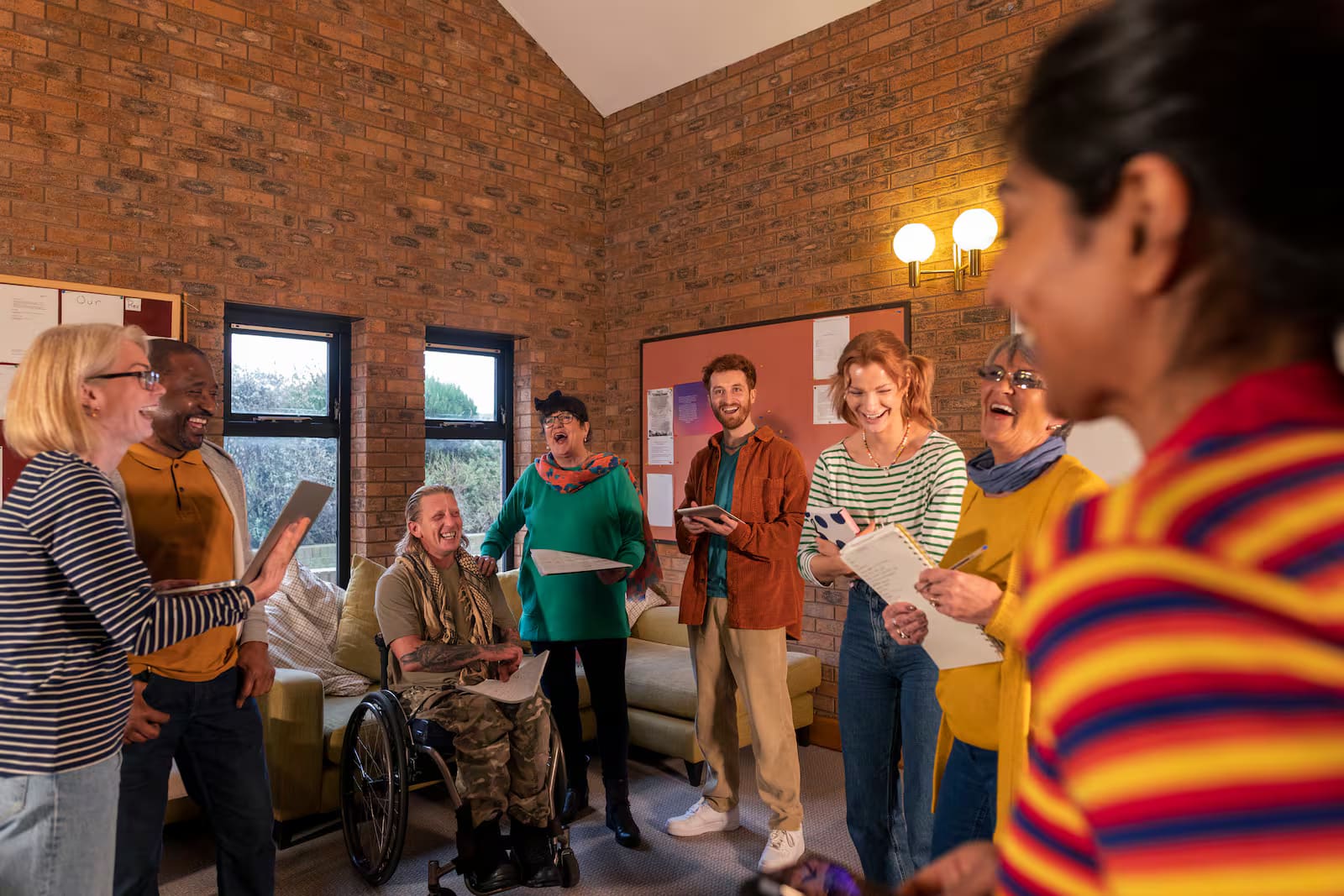 A mixed group of adults, including a wheelchair user, talking and laughing together during a group session.